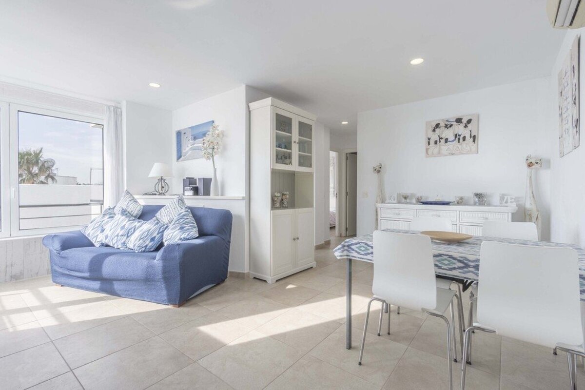 Bright, open-plan living and dining room with a blue sofa, white dining set, and tall storage cabinet.