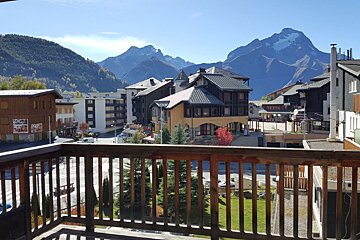 A scenic view of an alpine village with chalets and towering mountains in the background, captured from a wooden balcony.