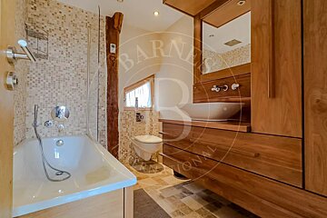 Rustic modern bathroom featuring a bathtub, wall-mounted toilet, wooden vanity with a vessel sink, mosaic tiles, and a wooden beam.