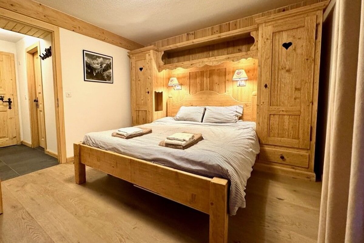 Cozy alpine bedroom featuring a wooden bed framed by rustic built-in wardrobes with heart cutouts.