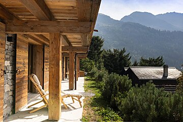 A wooden chair sits on a porch with mountains in the background