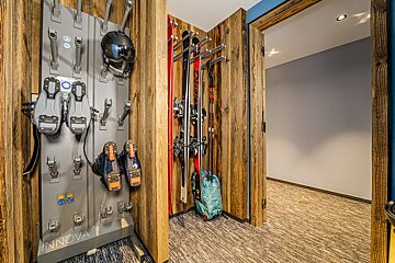 A rustic ski room features an Innova boot/helmet drying rack, skis, poles, and a backpack, all set against wooden walls.