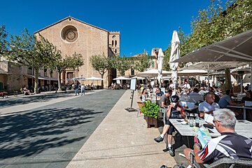 A group of people sit at tables under umbrellas in front of a church