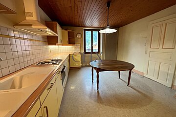 A kitchen featuring yellow cabinets, a wooden plank ceiling, and a round wooden dining table under a hanging pendant lamp.