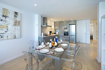 A dining room table with clear chairs in front of a kitchen