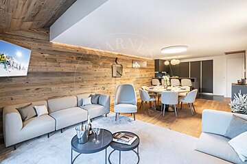 Elegant open-plan living, dining, and kitchen area with rustic wood walls, modern grey sofas, a dining table, and a contemporary kitchen.