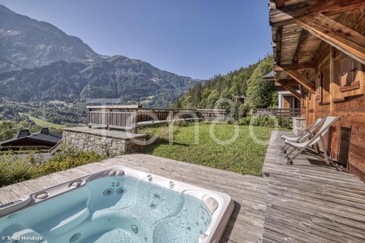 A hot tub sits on a wooden deck with mountains in the background