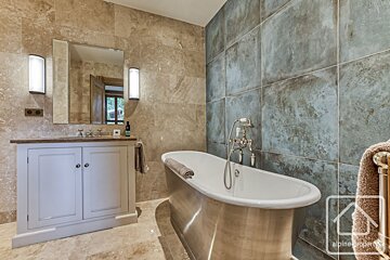 A luxurious bathroom features a freestanding tub, a light vanity, and contrasting tiled walls in warm brown and cool, textured grey-blue.