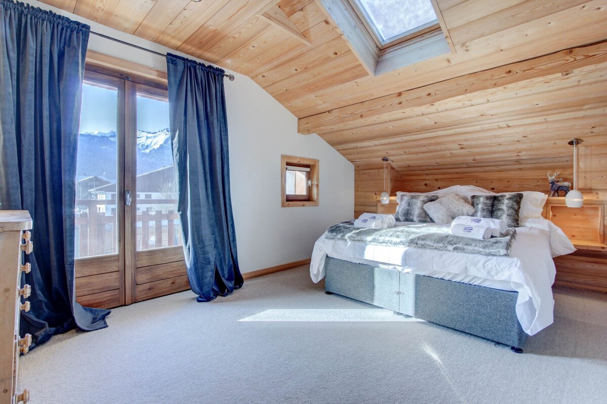 A bedroom with a bed and a window with mountains in the background