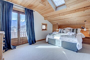 A bedroom with a bed and a window with mountains in the background
