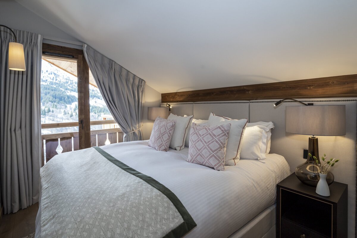 Cozy chalet bedroom with a large bed, stylish lamps, and a view of snowy mountains through the window.
