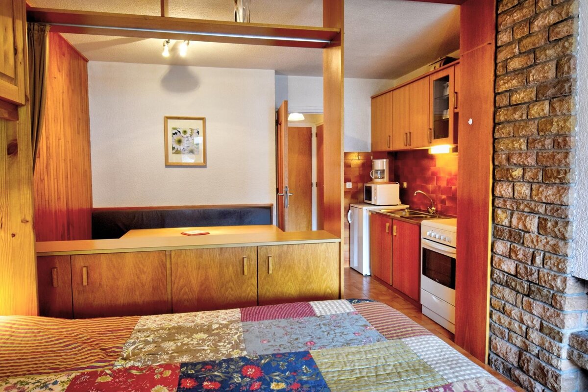 Cozy cabin-style studio featuring a bed with a patchwork quilt, wooden room dividers, a small dining nook, and a kitchen.