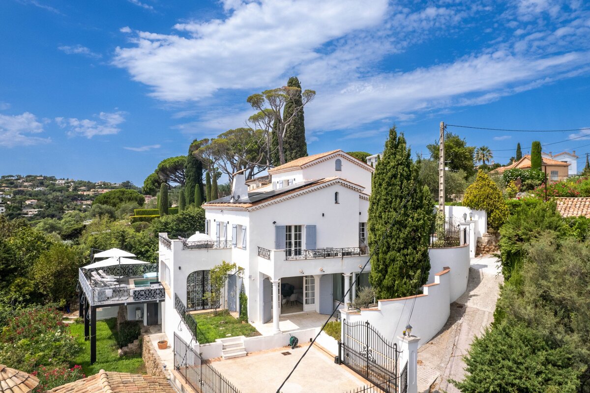 A large white house sits on top of a hill surrounded by trees