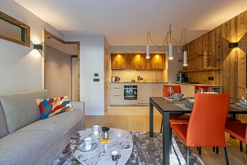 A modern, cozy apartment interior featuring a grey sofa, a marble coffee table, and a dining table with vibrant orange chairs.