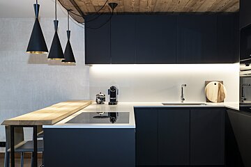 A modern dark navy kitchen with light wood accents, under-cabinet lighting, black conical pendant lamps, and a wooden ceiling.