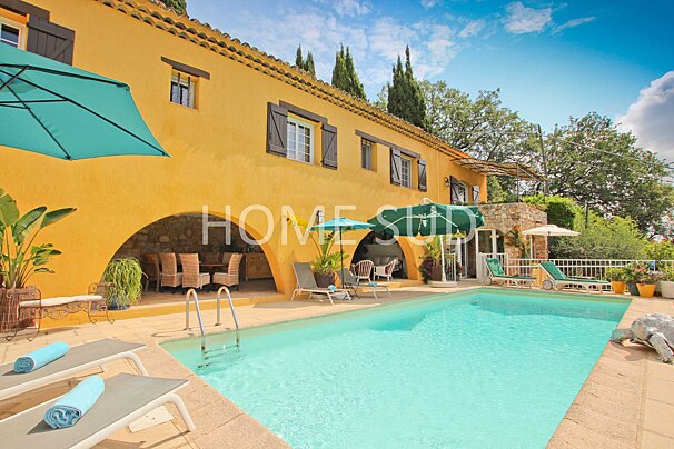 A large swimming pool in front of a yellow house that says home studio