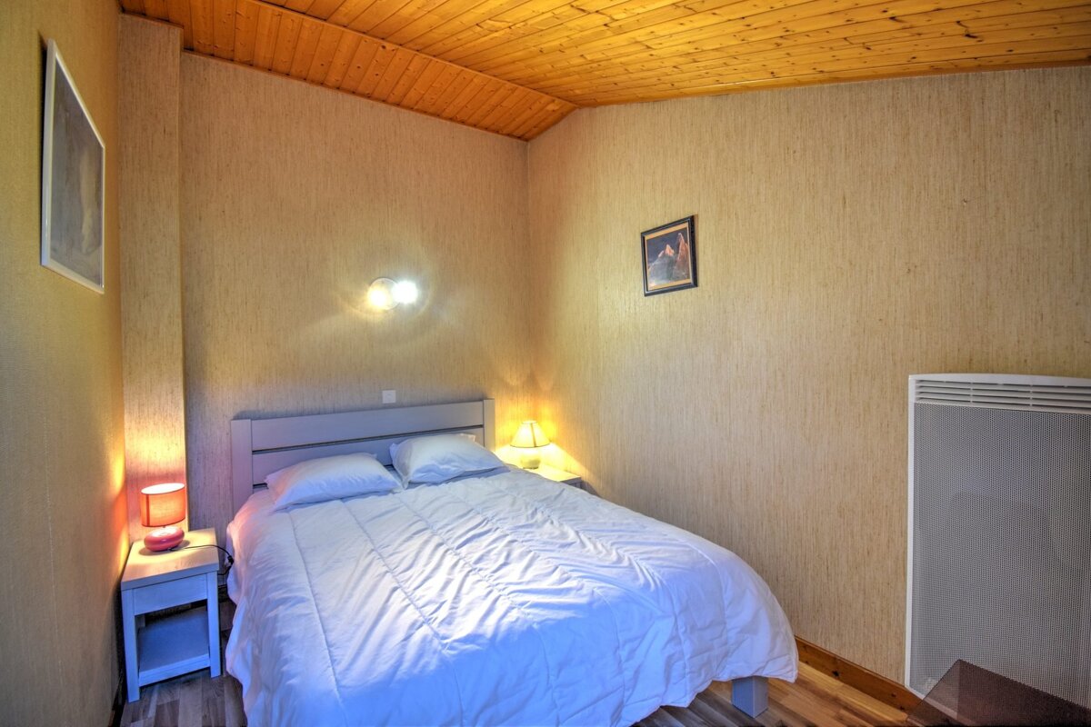 Cozy bedroom featuring a double bed with white bedding, bedside lamps, a slanted wood ceiling, and textured walls.