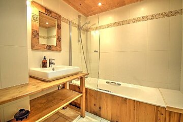 A rustic-style bathroom features a wooden ceiling, vanity, and tub paneling, white tiled walls with a mosaic border, and a shower-bathtub combo.