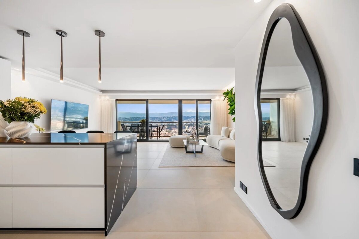 A modern, luxurious apartment interior with open living space, sleek kitchen island, and a wide balcony offering stunning city and mountain views.