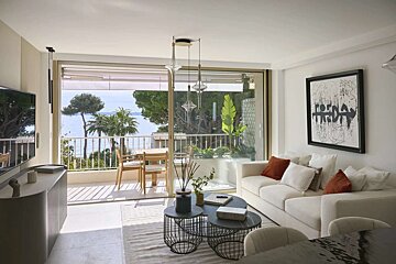 Bright, modern living room with an ocean-view balcony, palm trees, stylish furniture, and abstract art. Neutral tones.