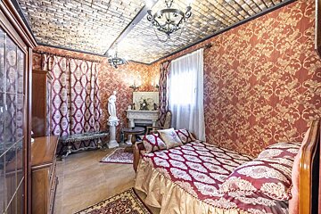 An opulent room with red and gold floral wallpaper, a unique brick-patterned ceiling, classic chandeliers, a fireplace, and an ornate bed.