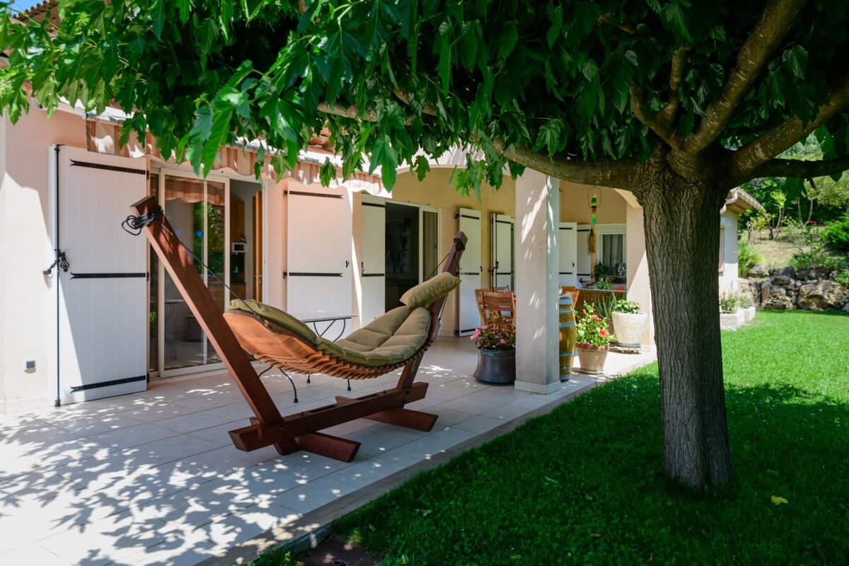 A hammock sits under a tree in front of a house
