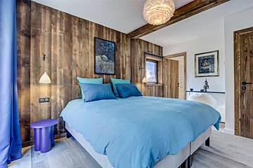 A bedroom with wood paneling and a blue bed