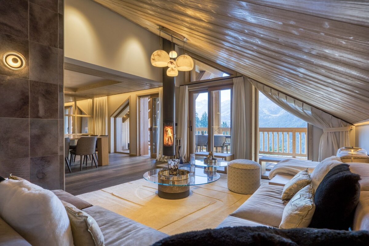 Luxurious chalet living room with a modern fireplace, vaulted wooden ceiling, and a balcony offering stunning mountain views.