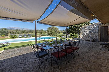 A table and chairs under a canopy overlooking a swimming pool