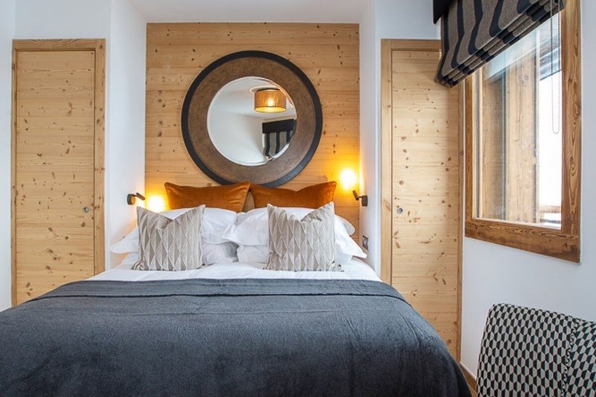 Cozy rustic bedroom featuring a wooden wall with a large round mirror, flanked by matching wooden doors, and a bed with grey bedding.