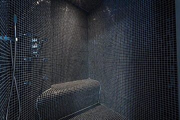 A modern shower room covered in black and white mosaic tiles, featuring a tiled bench and chrome fixtures.