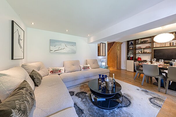 A modern, open-plan living and dining area with a large sectional sofa, coffee table, and ski-themed decor, adjacent to a set dining table and wooden shelves.