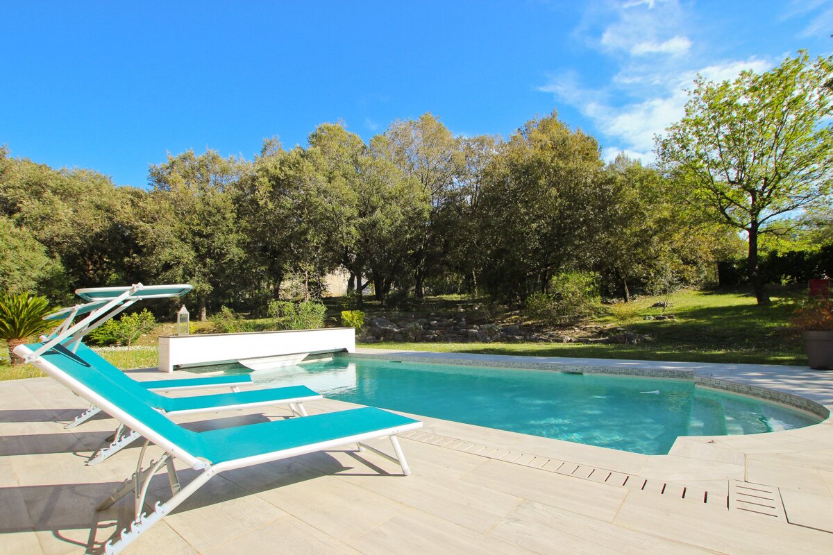A swimming pool surrounded by chairs and trees on a sunny day