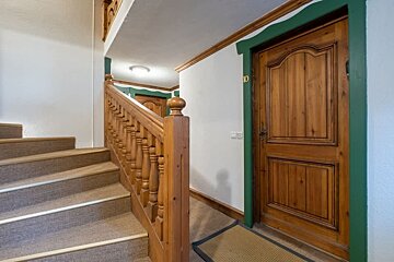 A rustic hallway featuring carpeted stairs with a wooden banister next to a wooden apartment door labeled 10 with green trim.