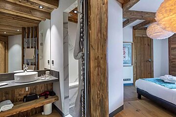 Chalet-style bedroom and modern open-plan bathroom with wooden beams, a vessel sink, shower, and fluffy pendant lights for a rustic yet luxurious feel.
