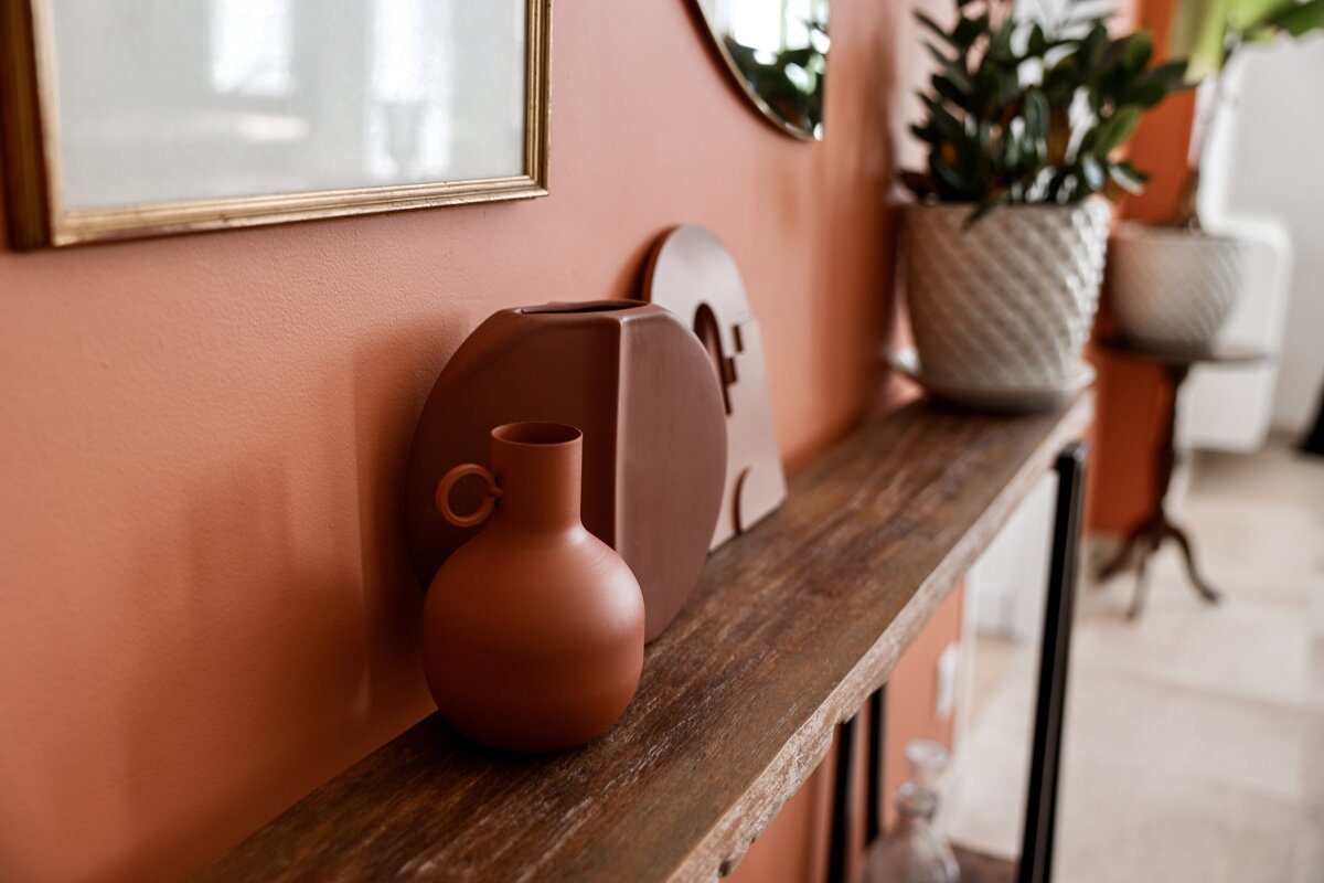 A vase sits on a wooden table in front of an orange wall