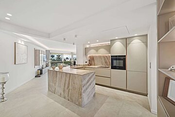 Bright, open-concept modern kitchen with a striking marble island and light cabinetry. It offers an expansive view of palm trees and outdoors.