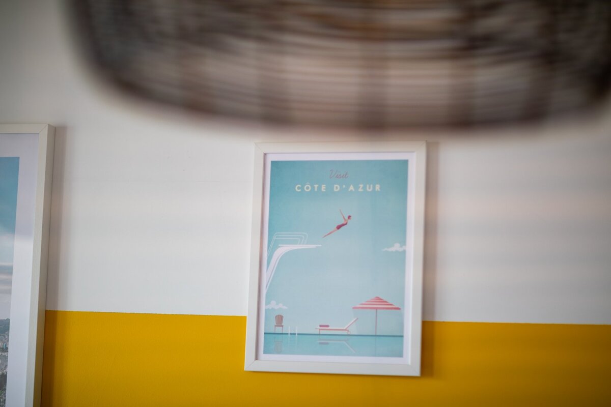 A framed picture of cote d' azur hangs on a yellow and white wall