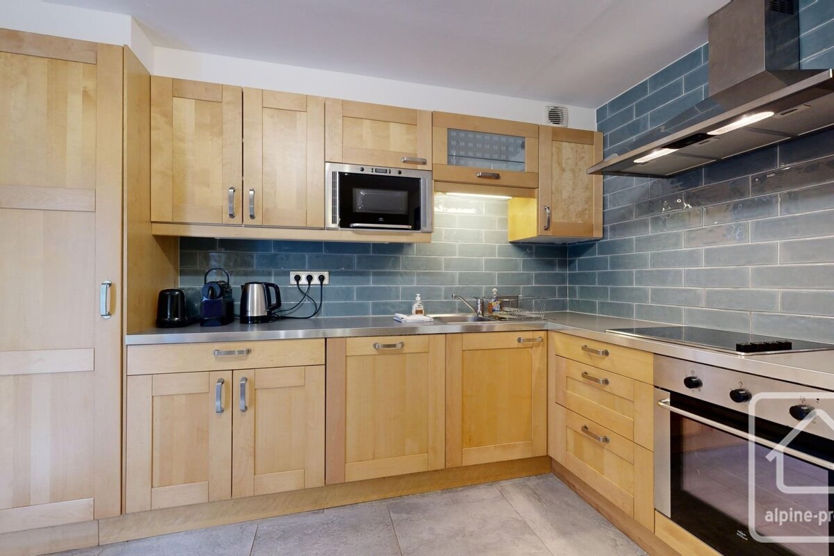 A modern kitchen with light wood cabinets, stainless steel appliances, and a blue subway tile backsplash.