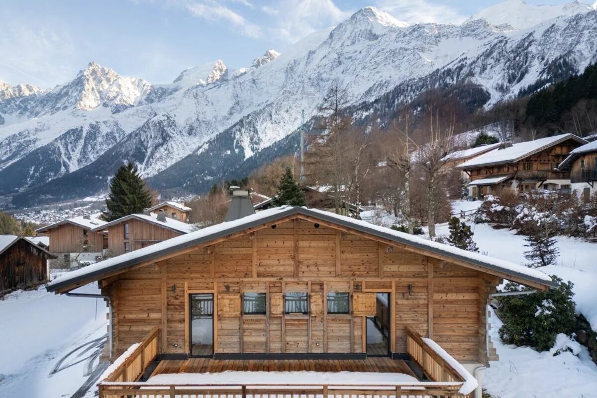 Wooden chalets in a snow-covered mountain village with high, snow-capped peaks in the background.