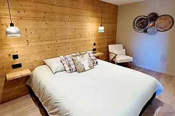 Cozy bedroom with a wooden plank accent wall, white bed with a deer pillow, hanging lights, a white armchair, and decorative wall art.