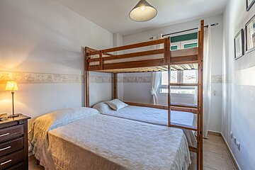 A cozy bedroom features a wooden bunk bed, a single bed, white walls with a playful border, a glowing lamp, and a window.