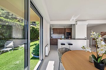 Stylish open-plan kitchen and dining area with a view of a lush green patio through large sliding glass doors.