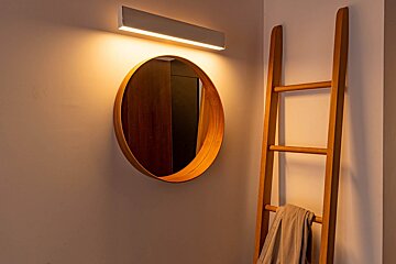 A round mirror hanging on a wall next to a wooden ladder