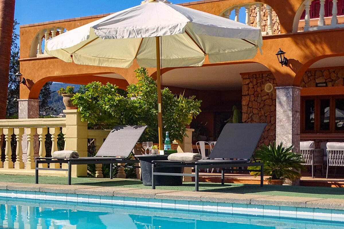 Two lounge chairs under an umbrella next to a swimming pool