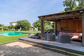 A wooden gazebo with a pool in the background