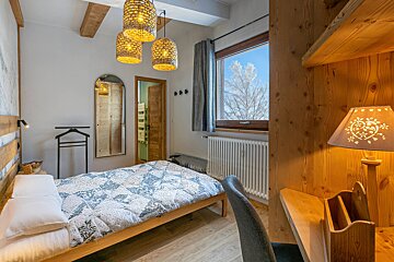 Cozy cabin bedroom with wood paneled walls, woven pendant lights, a patterned quilt, and a window with a snowy view.