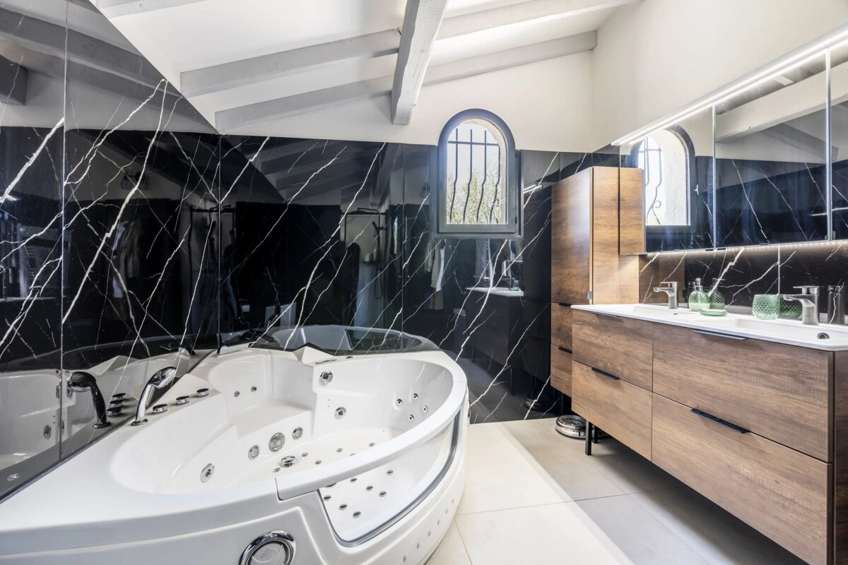 Modern bathroom featuring a large white jacuzzi tub, black marble walls, and a wooden vanity.