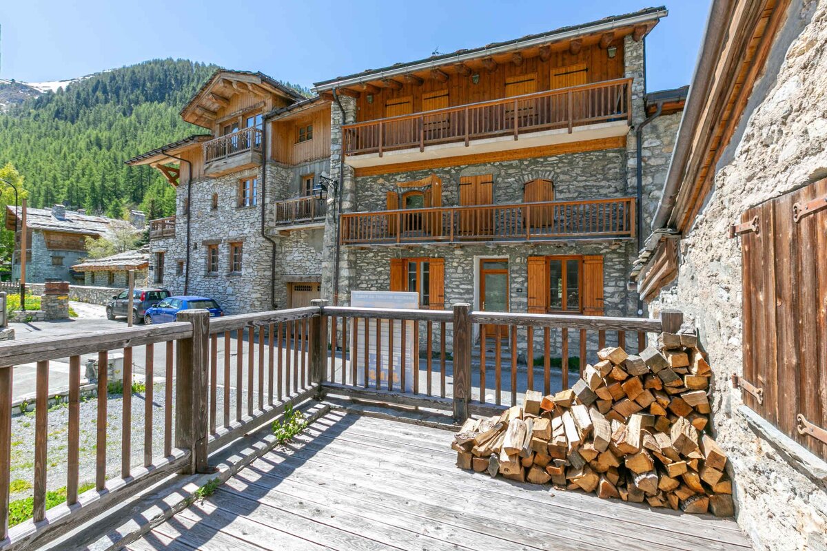 Rustic alpine chalets made of stone and wood, with a pile of firewood on a wooden deck in the foreground.