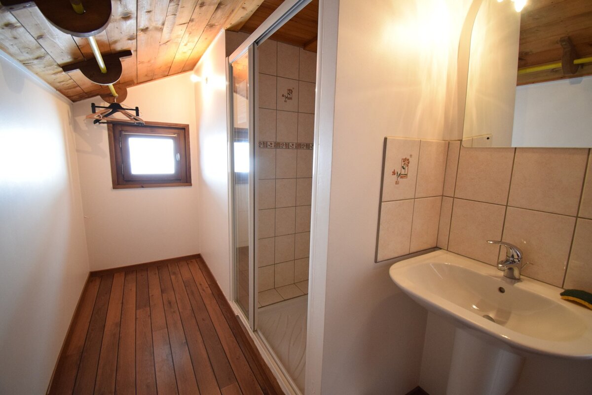 Bathroom with a wooden ceiling and floor, featuring a pedestal sink, tiled glass shower, and a small window in a narrow nook.